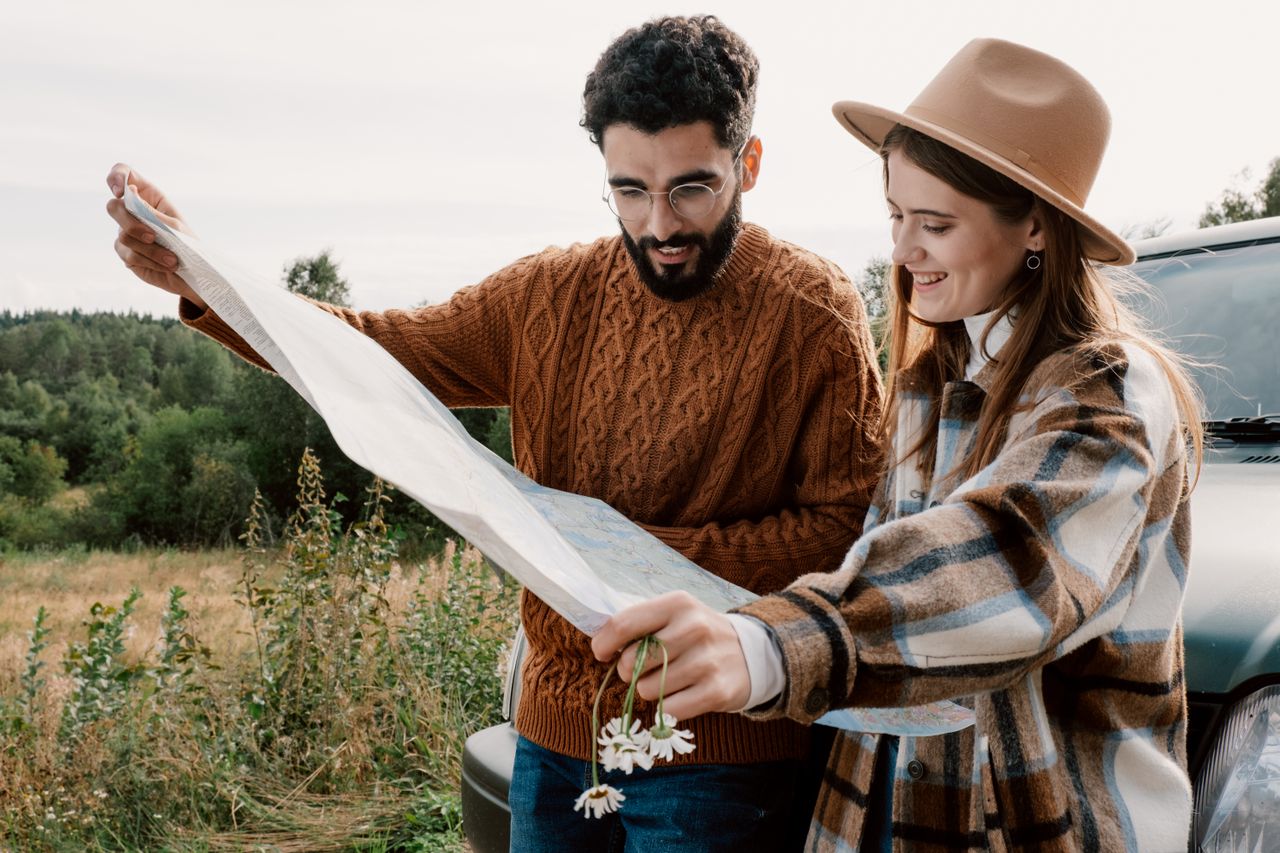 Two travelers studying a paper map beside their vehicle