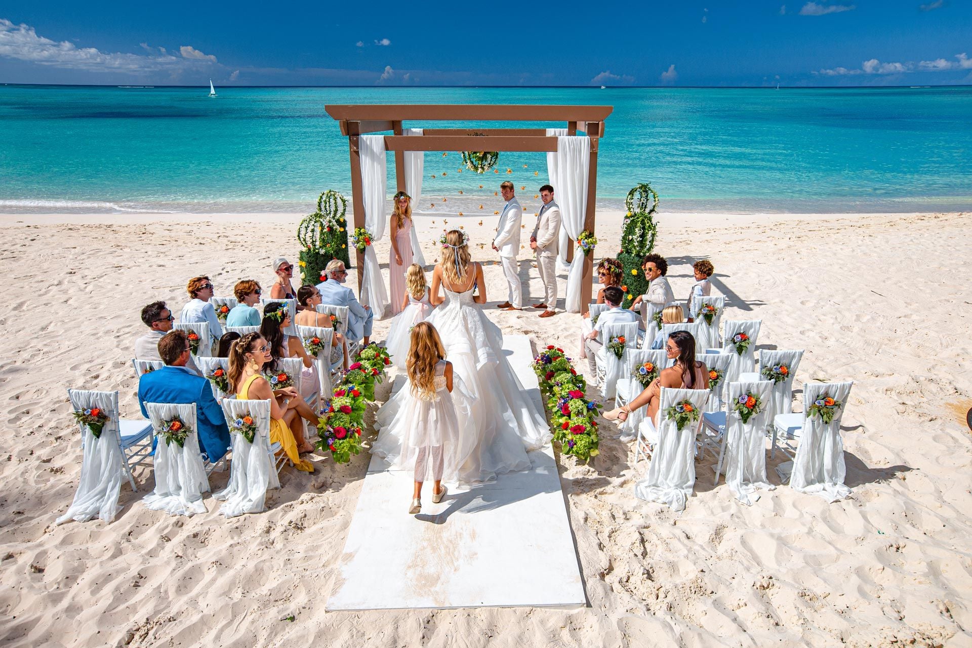 A beach wedding ceremony on white sand beside turquoise water