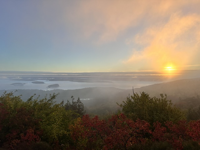 Golden sunrise over misty islands and autumn-colored foliage from an elevated viewpoint in Acadia