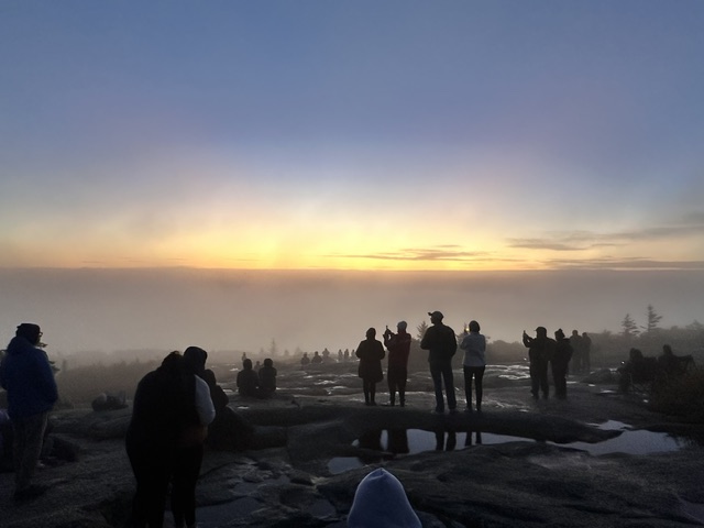 Visitors silhouetted on a rocky summit beneath a foggy sunrise